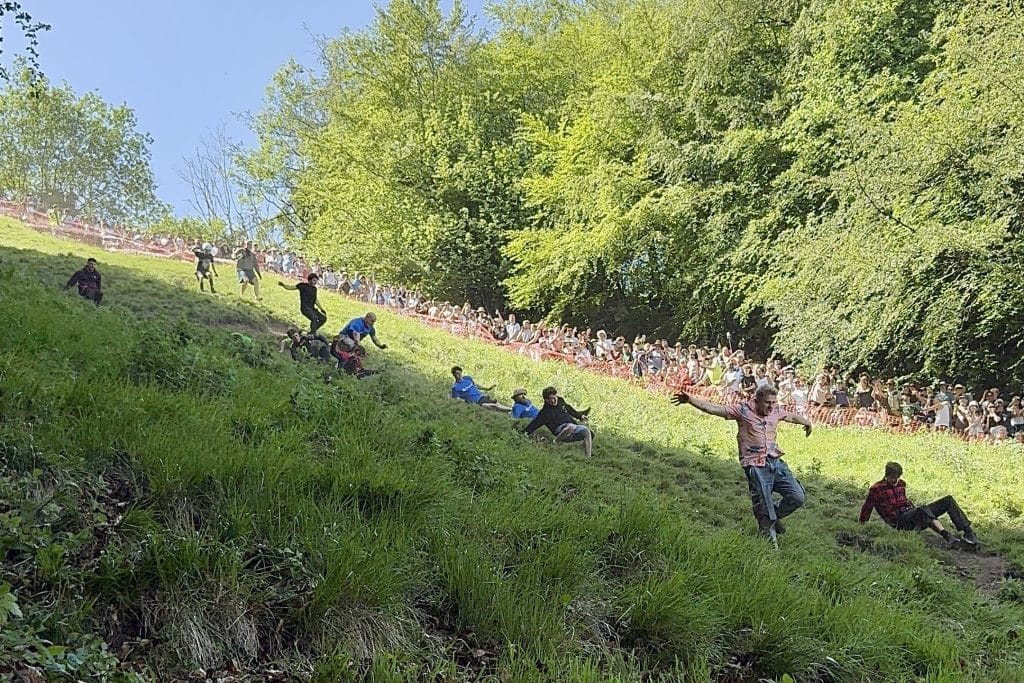 A group of men running down the hill, chasing the cheese.