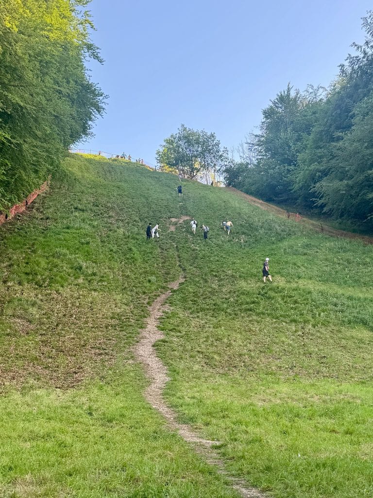 A bright green empty super steep hill with only a few people on it.