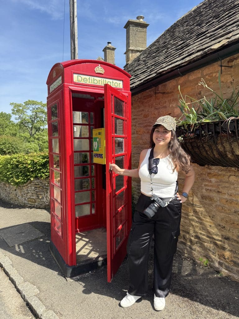 Kate standing in front of a traditional British red phone booth, which now contains a defibrillator instead of a phone.
