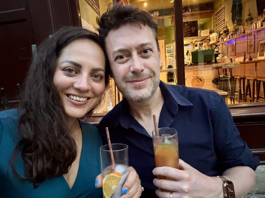 Kate and Charlie take a smiling selfie while holding cocktails.
