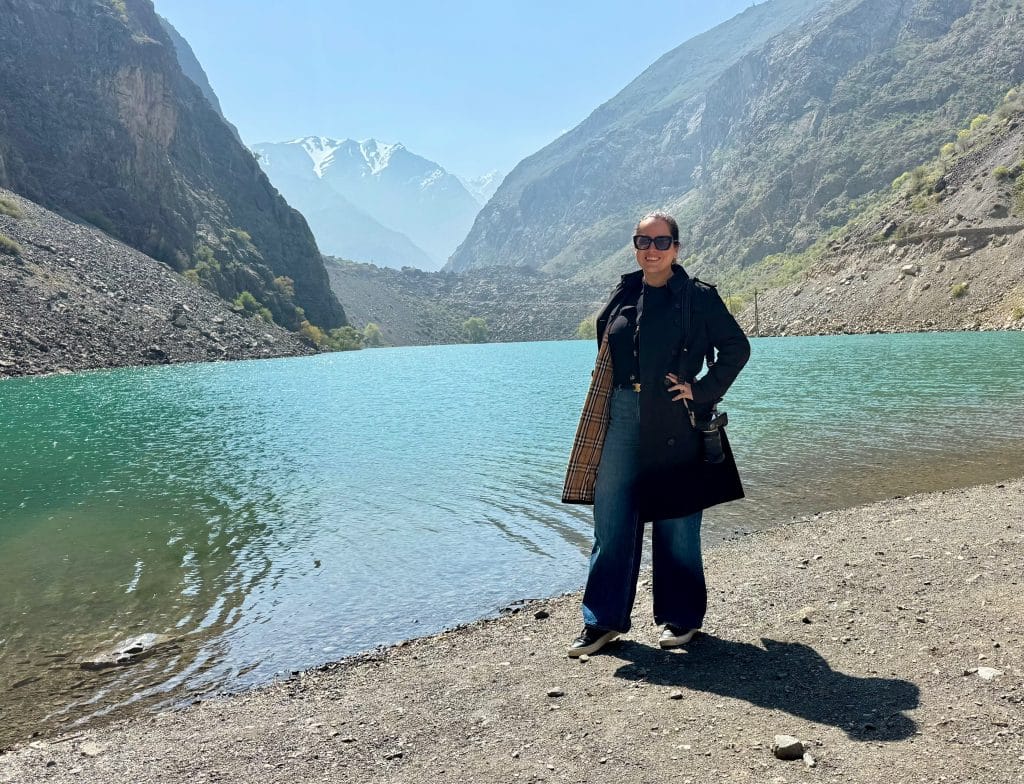 Kate standing in front of a turquoise lake with mountains behind her.