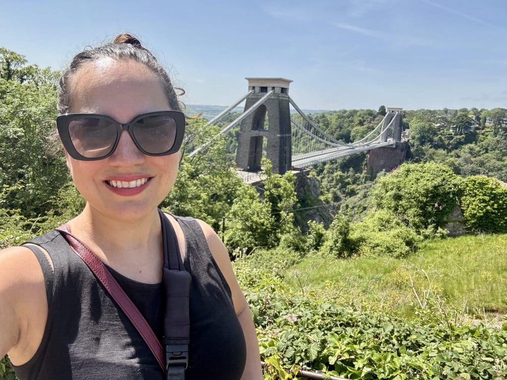 Kate stands in front of a large suspension bridge in Bristol, UK.