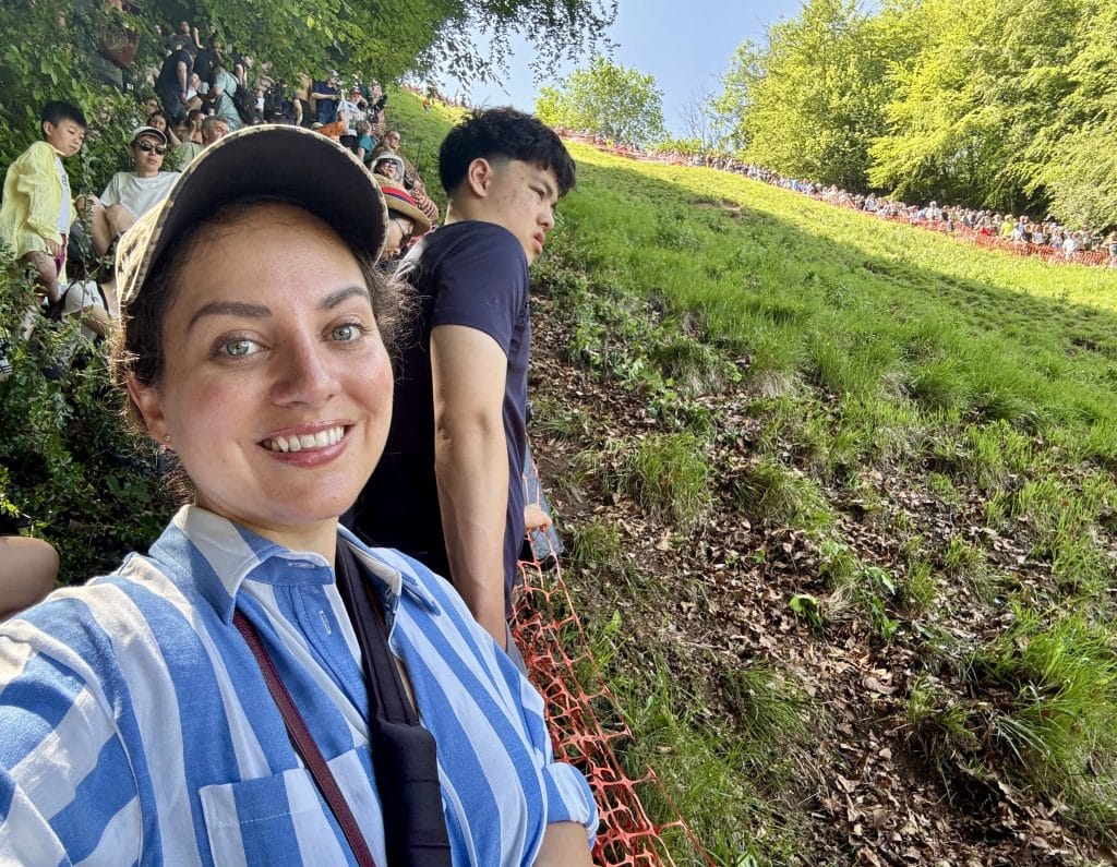 Kate taking a smiling selfie while standing next to the hill.