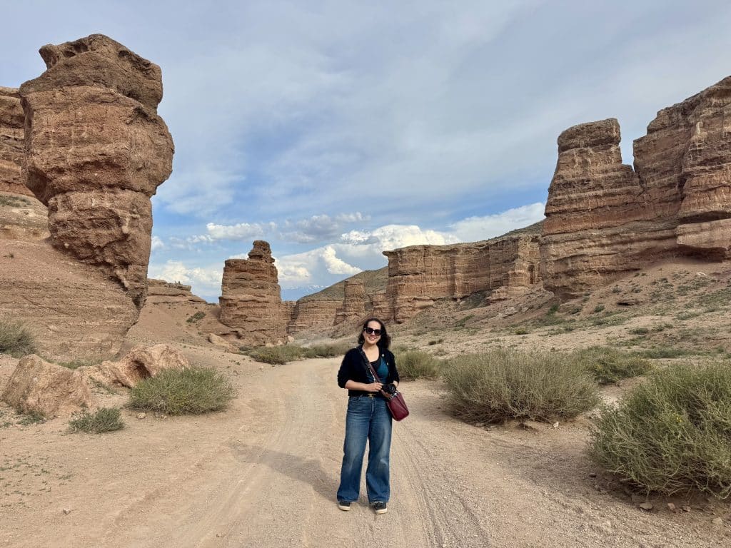 Kate standing on a dirt road in a canyon, large rock formations on each side.