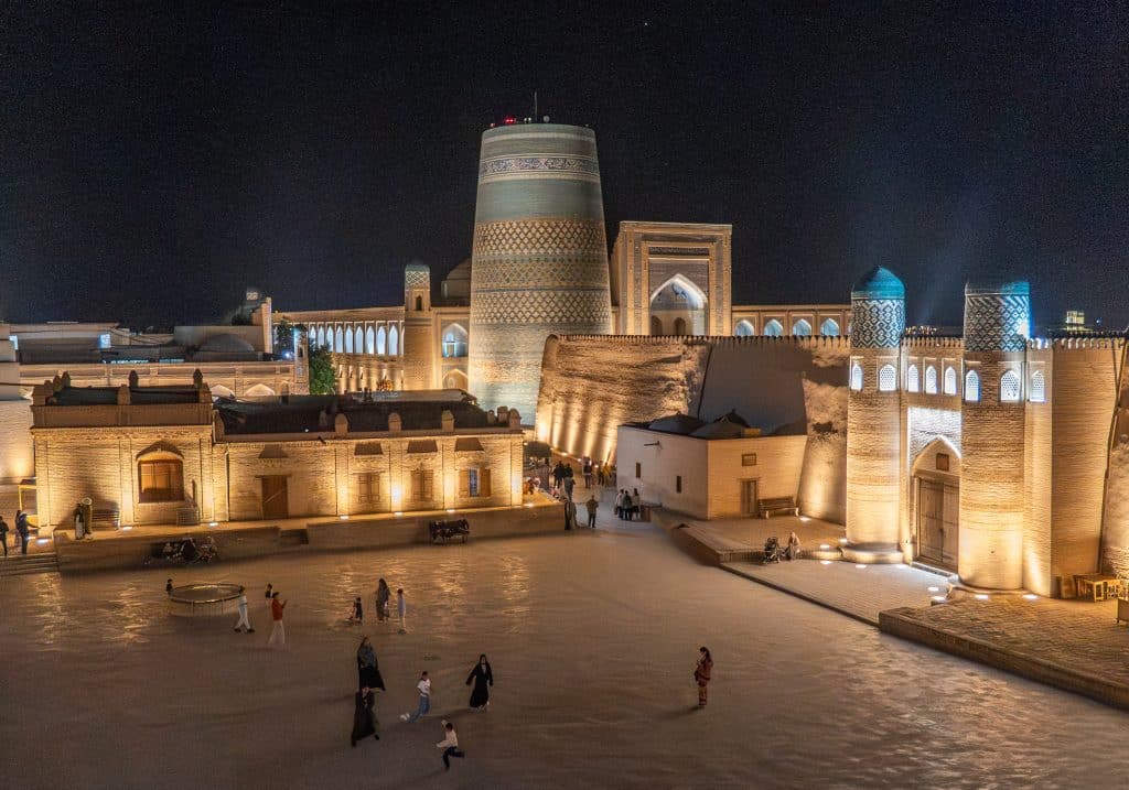 The sand-colored castles with turquoise domes in Khiva, lit up at night as kids play soccer in front of them.