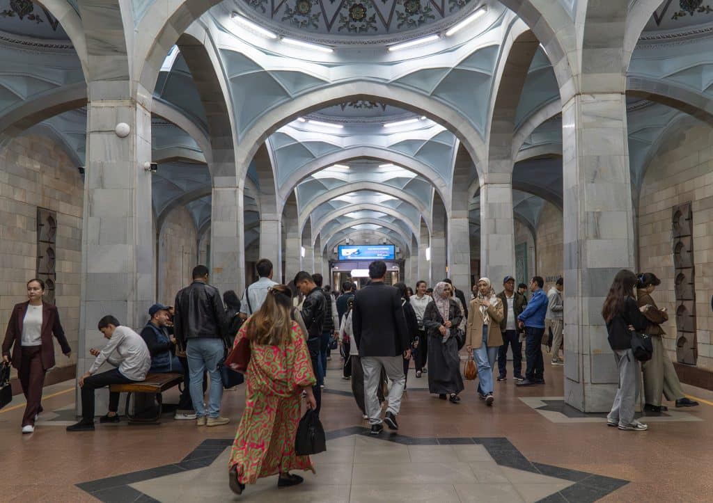 A subway station with a ceiling shaped like a mosque, with curves and geometric patterns, as dozens of people pass through.