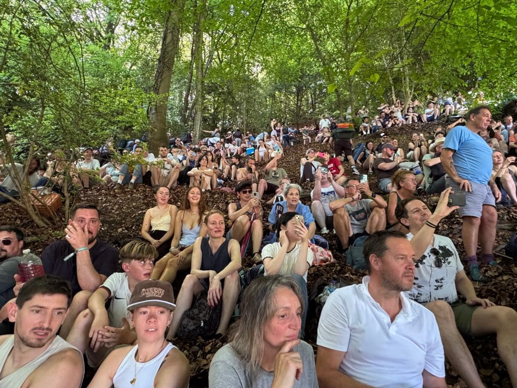 A group of people sitting on the hill beneath tree cover.