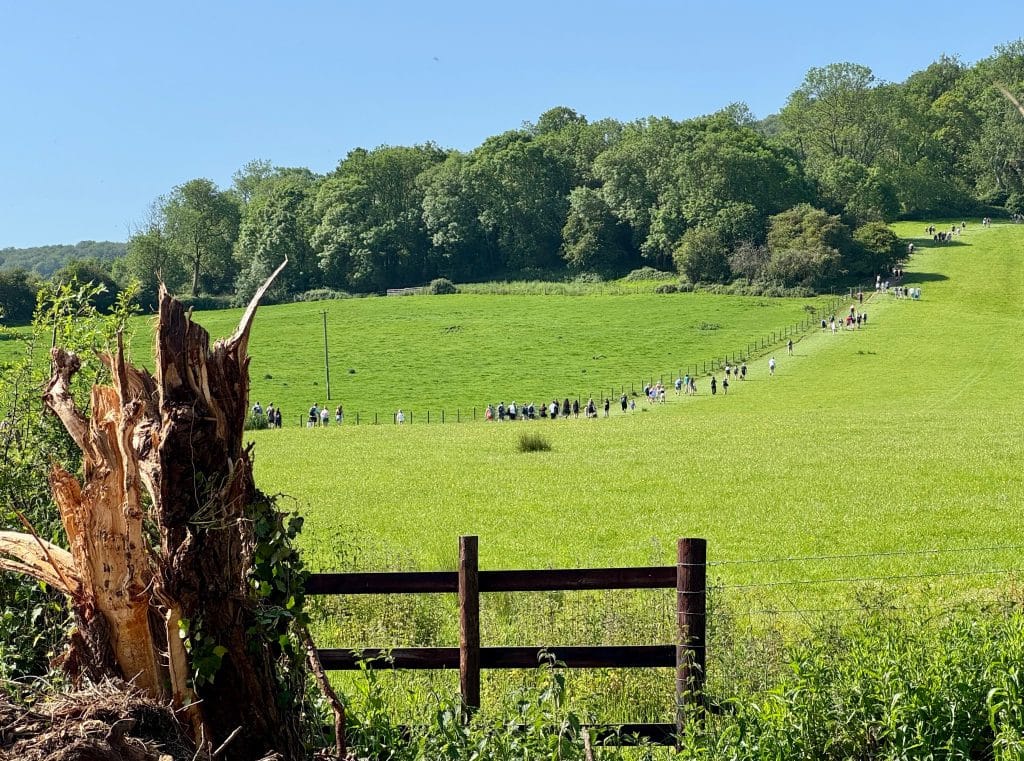 A long line of people walking up a grassy hill.