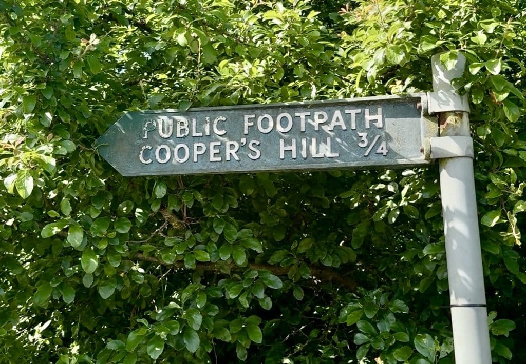A sign tucked among trees reading Public Footpath Cooper's Hill 3/4.