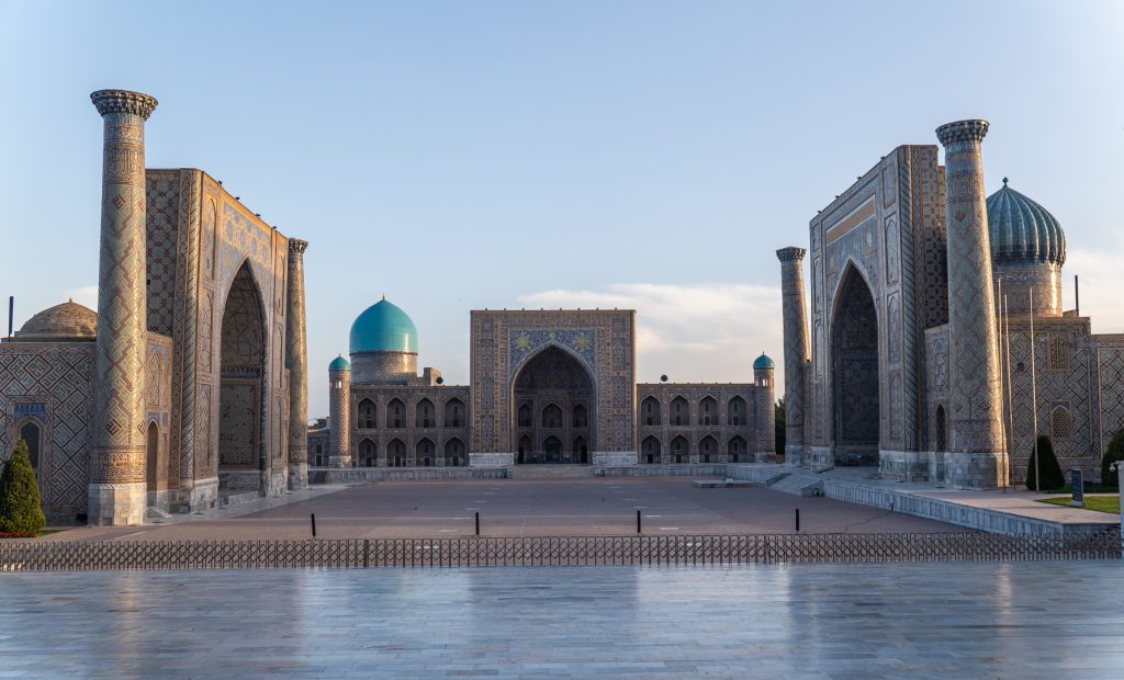 Samarkand's Registan, with three gorgeous religious buildings lit up in early morning light against a blue sky.