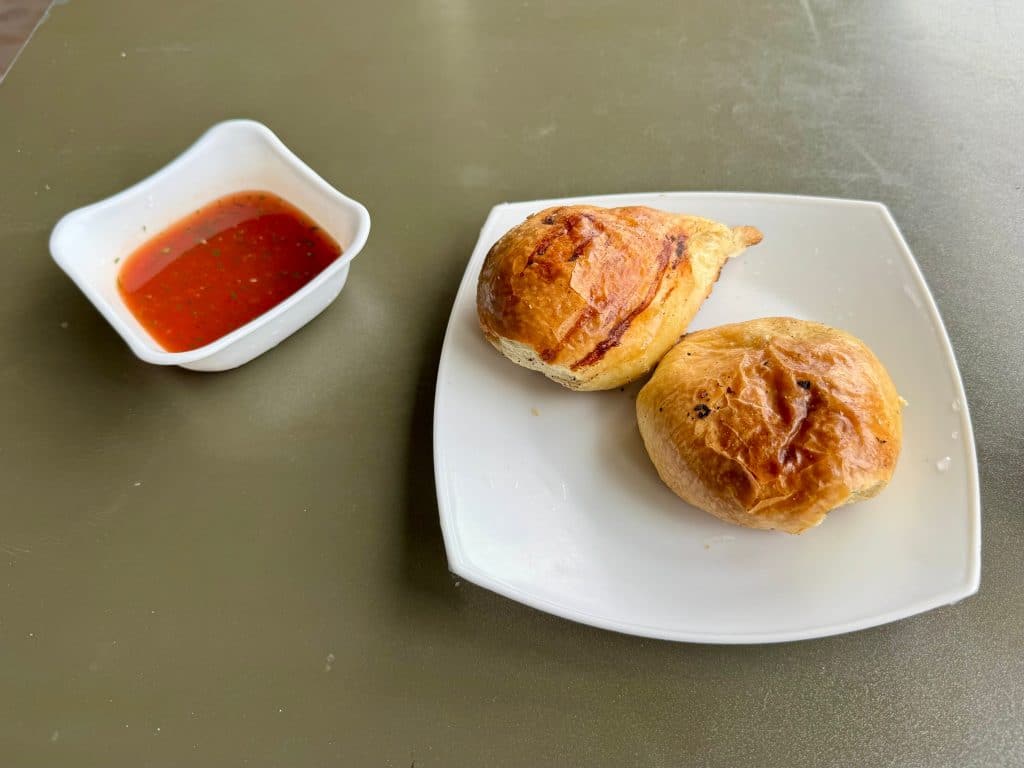 A plate with two round pastries on it next to a ramekin of red sauce.