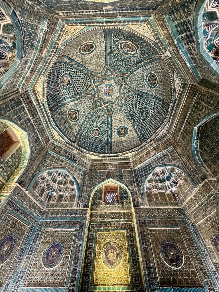 The inside of a mausoleum in Samarkand, with lots of geometrically patterned mosaics in blue, turquoise, and white.