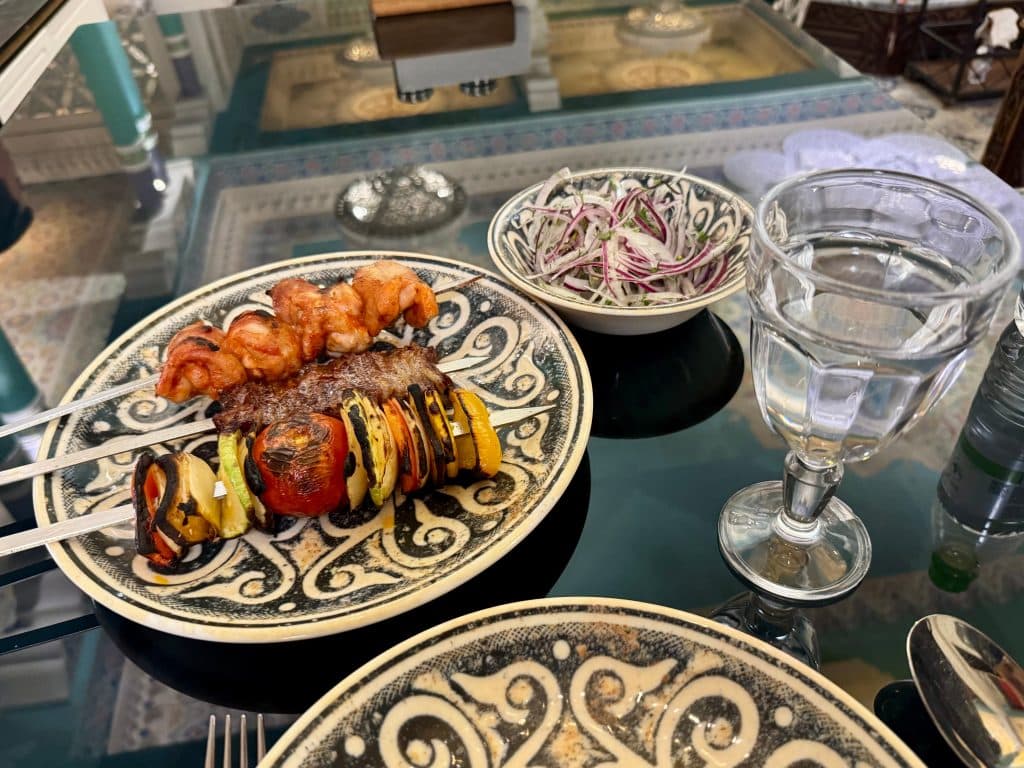 A plate with three pieces of shashlik: a vegetable kabob, a chicken thigh kabob, and a beef kabob.
