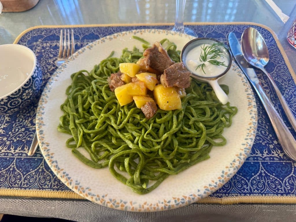 A plate of green noodles topped with potatoes and a few chunks of beef.