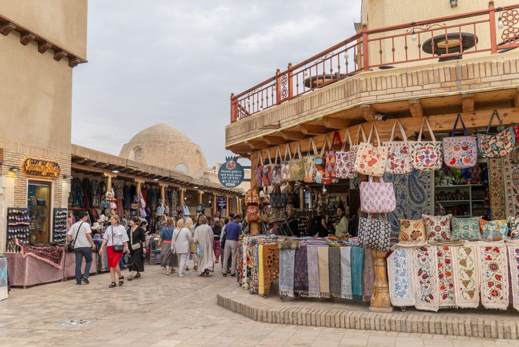 Shops in Bukhara with outdoor displays of embroidered wall hangings and tote bags.