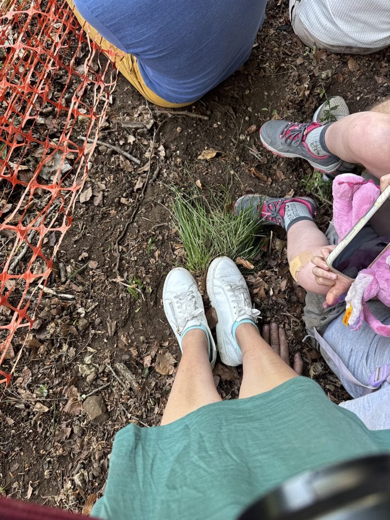 Kate's white sneakered feet perched on a tiny tuft of grass, surrounded by dirt.