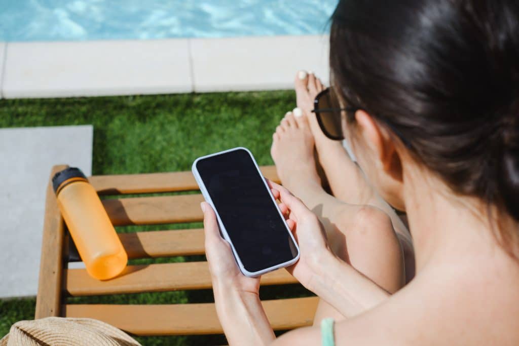 A woman looking at her phone while sitting by the pool.