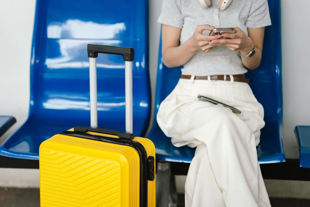A woman sitting in a seat on her phone, a yellow suitcase next to her.
