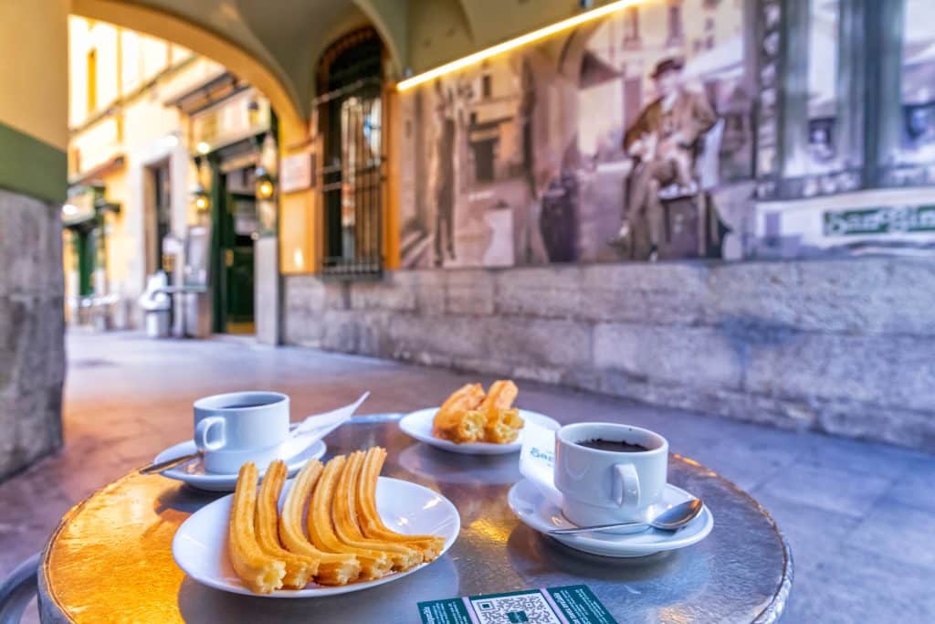 Traditional Spanish breakfast with hot chocolate and churros on an outdoor terrace.