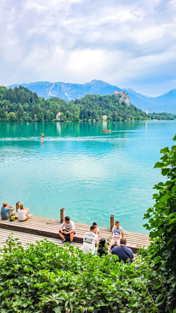 people sitting beside lake bled with castle in backgroud