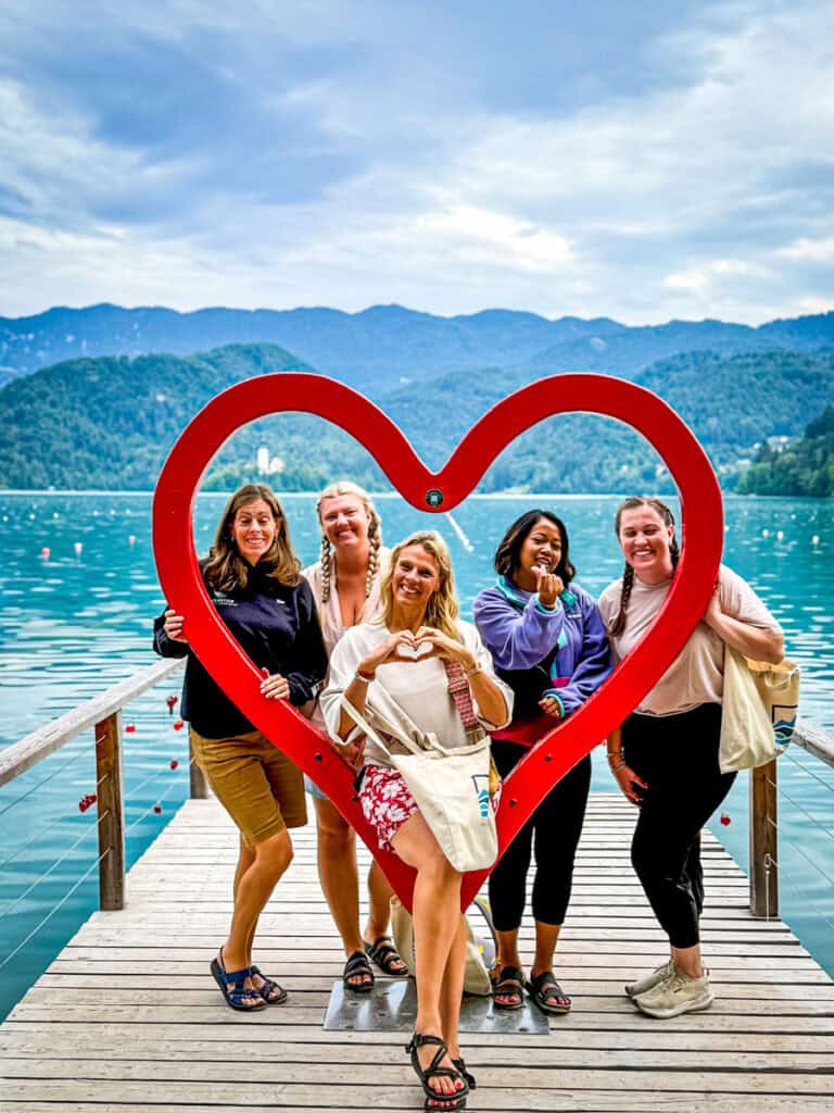 women taking photo with heart sculpture lake bled