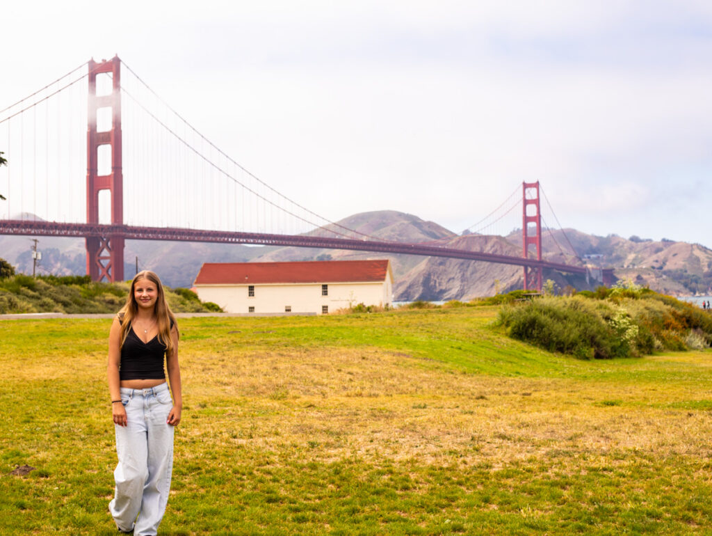 girl standing in front of golden gate bridge on grassy field