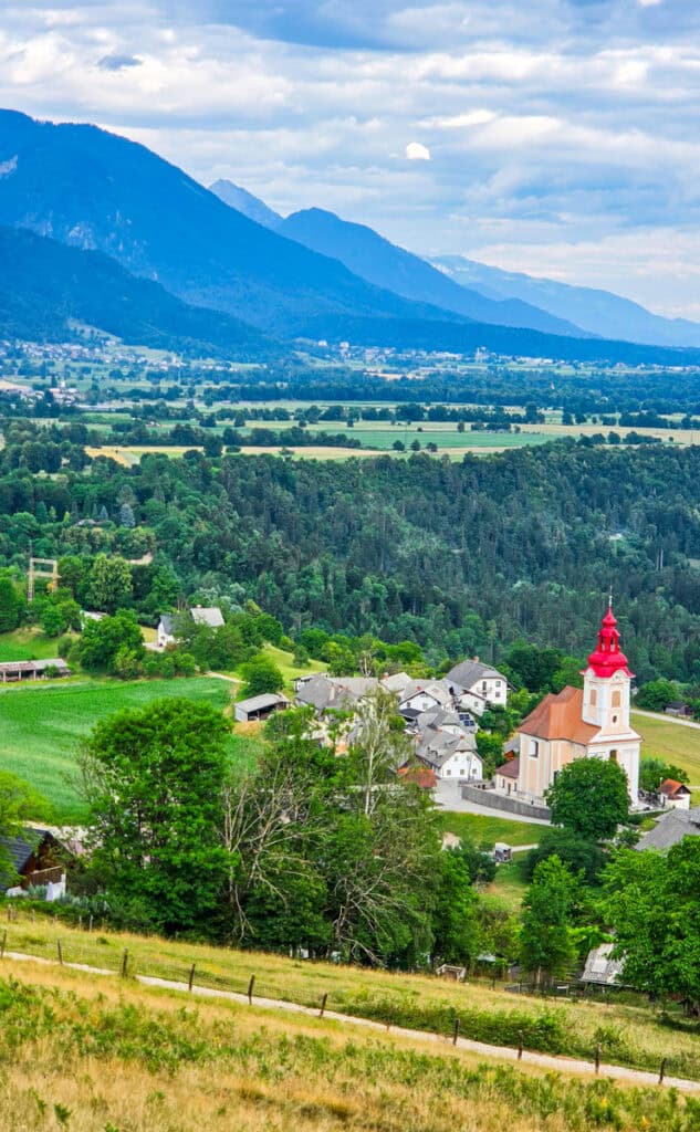 valley with mountains in background and red steepled church near vintgar gorge